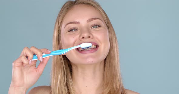 Woman with Adorable Smile Brushing Her Teeth, Isolated on Blue Background alt