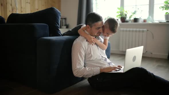 Father Is Trying To Work on Laptop with His Son Cuddling Him in Living Room