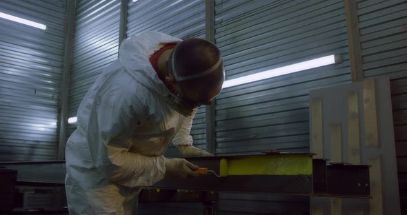 Man in Overalls and Protective Mask Paints Metal Structures with a Roller Yellow alt