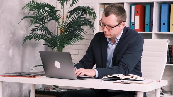 Slow Motion of the Side View of a Serious Businessman in Glasses and a Suit Sitting in the Office at alt