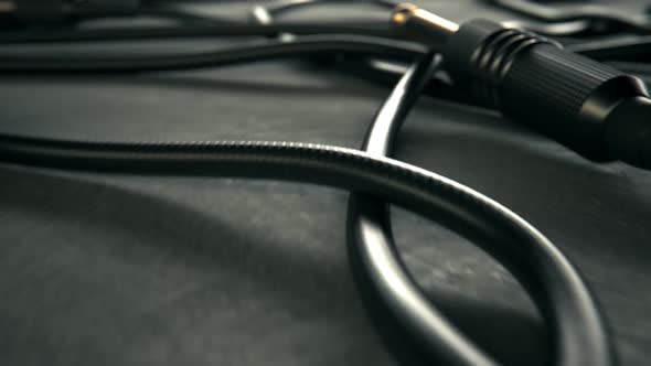 Bunch of tangled black audio cables with jack plugs lying on grey studio floor. alt