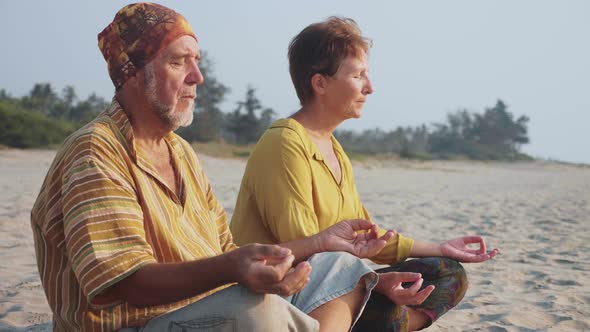Senior Couple Sits and Meditating Together on Sandy Beach alt