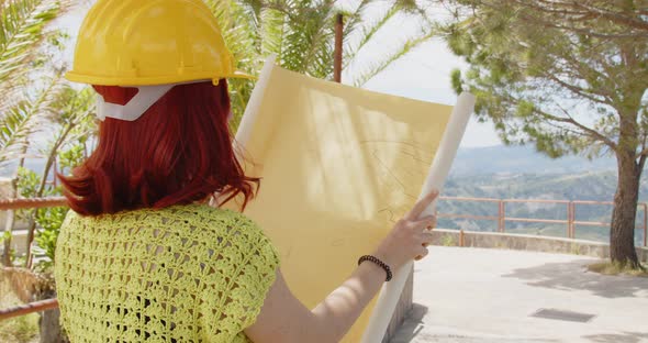 Female engineer looking at the project in the mountains with a yellow helmet alt