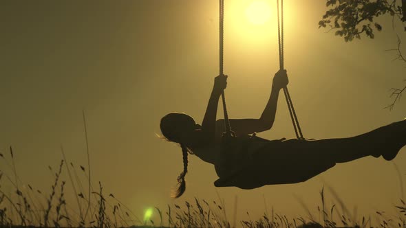Child Swinging on a Swing in Park in Sun. Ilhouette of a Small Healthy Child on a Swing. Teen Girl alt