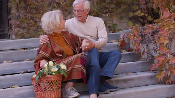 Handsome senior couple sitting on stairs with basket full of flowers and groceries