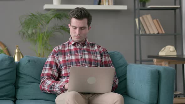 Man with Laptop Smiling at Camera on Sofa alt