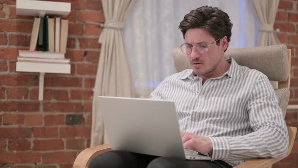 Middle Aged Man with Laptop Reacting to Loss on Sofa alt