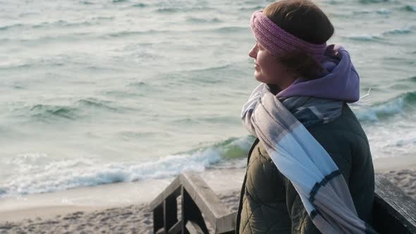 Woman in Warm Clothes Breathes Fresh Air on the Beach in Winter alt