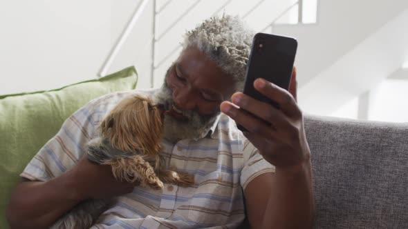 Senior man holding his dog having a video chat on smartphone at home alt
