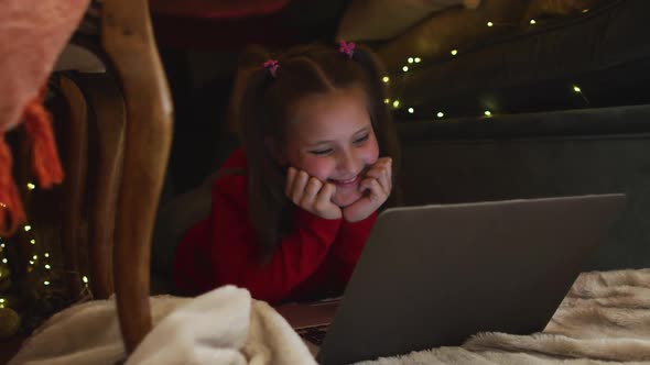 Caucasian girl smiling while using laptop under blanket fort during christmas at home alt