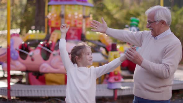 Grandfather having fun with his cute little granddaughter in the amusement park