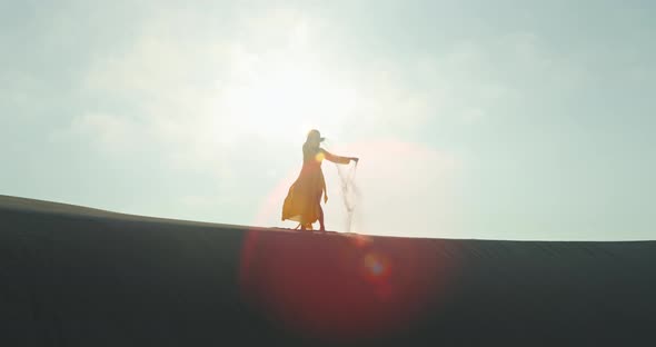 Silhouette of Woman Dispelling Sand in Air From Hands alt