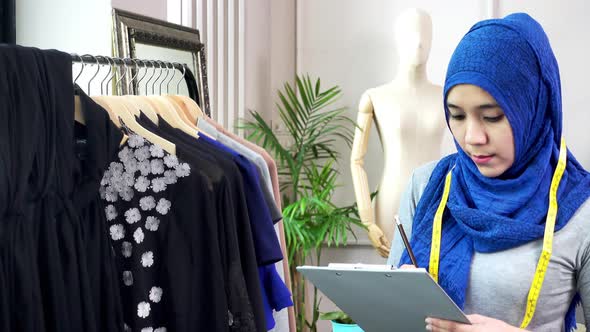 Asian muslim woman designer as a startup business owner checking clothes on the rack