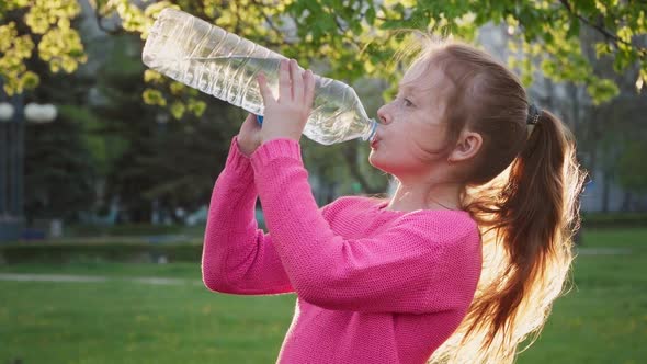 Ginger Little Girl Drinking Water From Bottle in Sunny Summer Park