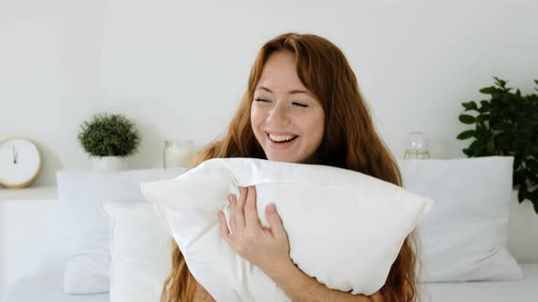 Happy beautiful woman is sitting on bed in morning clutching a soft pillow