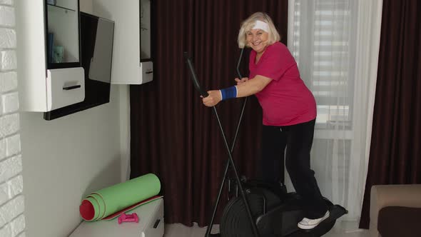 Healthy Elderly Senior Grandmother Model Exercising Sport Workout on Orbitrek in Room at Home alt