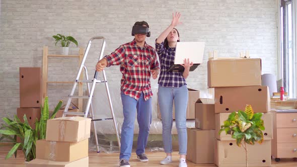 Young Woman with a Laptop Shows a Man in VR Glasses the Project of a New Apartment alt