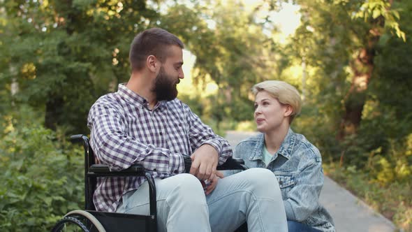 Young Caucasian Couple in the Park Disabled Person Man is Sitting Wheelchair and Woman Who Loves Him alt