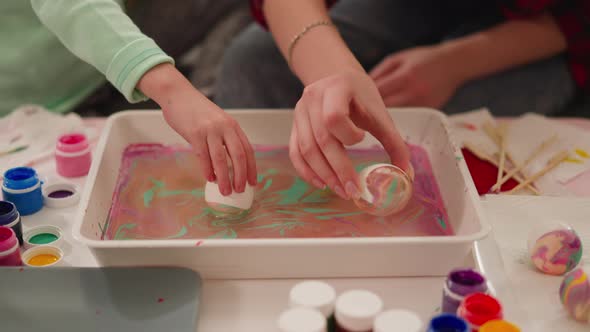 Mother and Girl Roll Eggs in Tray with Paints and Oily Water alt