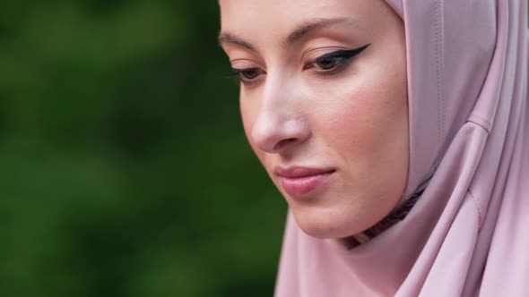 A close-up side view of an arabian woman wearing pink national hijab is using her laptop alt