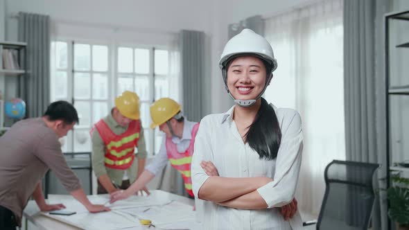 Woman Engineer With Helmet Crossing Arms And Smiling To Camera While His Colleagues Working alt