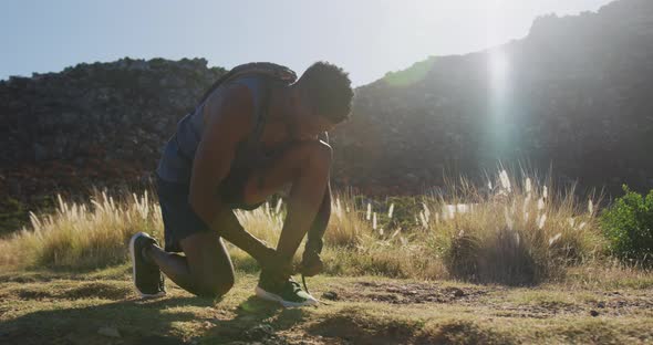 African american man exercising outdoors tying his shoe in countryside on a mountain alt