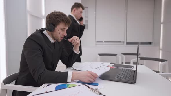 Side View of Busy Handsome Caucasian Man Conferencing Online As Colleague Talking on Phone Walking alt