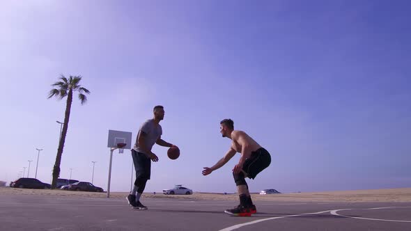 A man takes a layup shot while playing one-on-one basketball hoops on a beach court alt