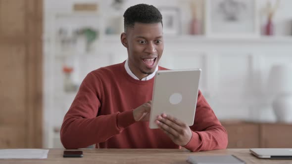 African Man Celebrating Success on Tablet in Office alt
