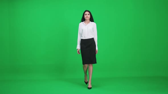 Female in a Suit Walks on a Green Background Businesswoman Comes Closer and Looks at the Camera alt