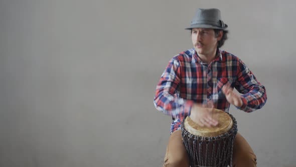 Funny Man with a Mustache and a Hat Playing the Ethnic Drum