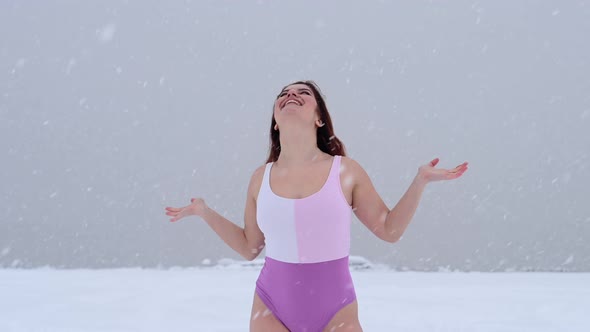A Happy Woman in a Swimsuit Catches Falling Snowflakes Near a Frozen Lake alt