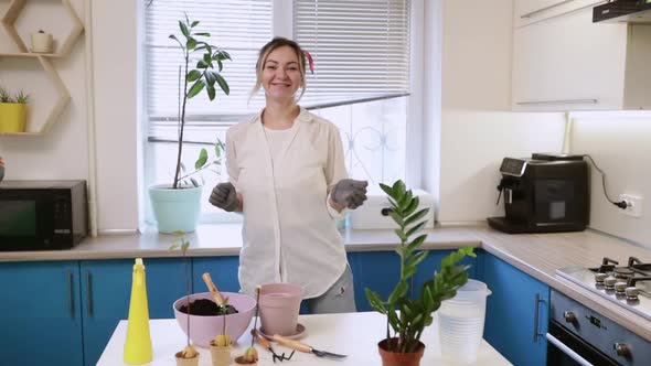 A Cute Girl Transplants a Plant at Home While Dancing Funny in Gardening Gloves alt