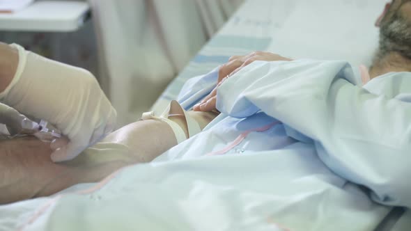 Close up shot of nurse hands inserting IV needle into veins of a patient alt