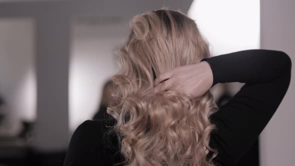 Blonde Straightens Her Hair with Her Hand Showing the Styling of the Wavy Curls alt
