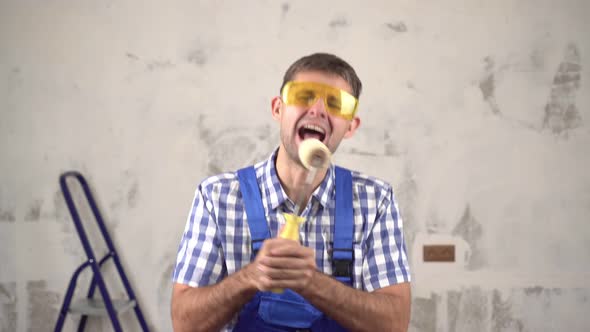 Cheerful Funny Male Builder Sings and Dances on Background of Repairs in House alt