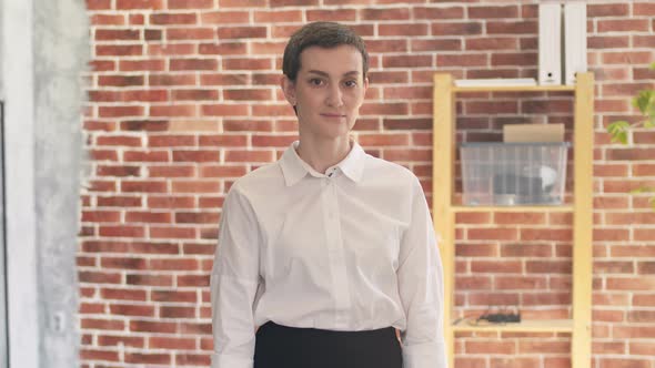 Short-haired confident woman crosses arms on chest, looking at the camera and standing in the office alt