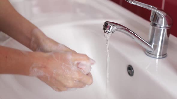 Woman Washes Her Hands in the Bathroom with Water Soap and Foam alt