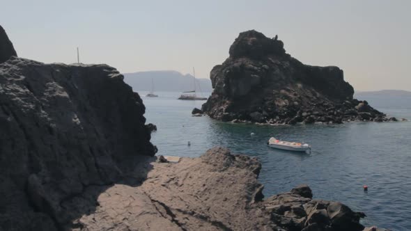 A rocky beach within the Santorini caldera with catamarans floating around it. alt