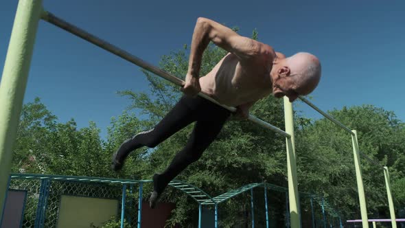 Old Man with Bare Torso Does Exercise on Ground Crossbar