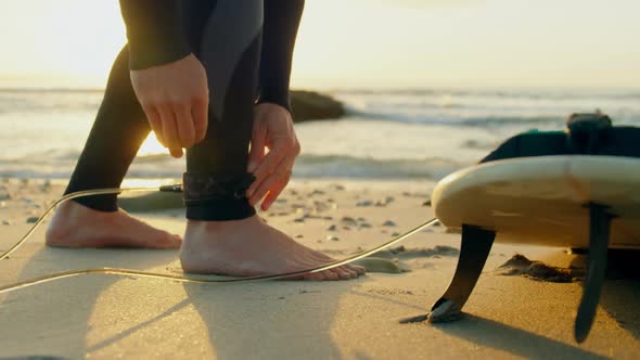 Low section of mid-adult caucasian male surfer tying surfboard leash at the beach 4k alt