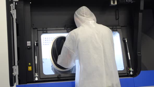 A Man in a White Protective Suit Stands Near a Large 3D Printer alt