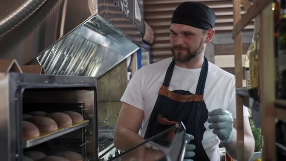 Catering, Attractive Male Chef Baker Takes Out Fresh Bun From Oven for Making Burger or Hamburger in alt