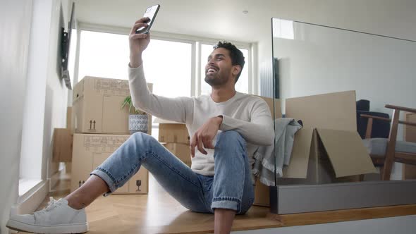 Man With Mobile Phone Moving Into New Home Making Video Call Surrounded By Boxes