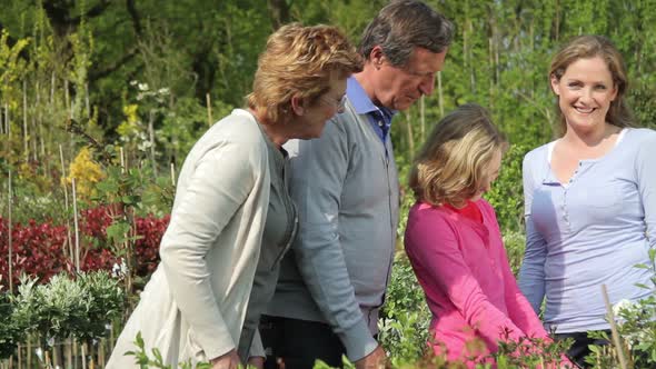 Grandparents, daughter and granddaughter looking at plants in garden centre alt