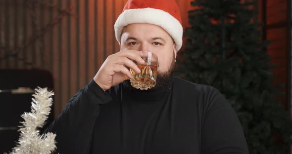 Man Preparing for Christmas Sitting at Home Wearing Santa Claus Costume alt