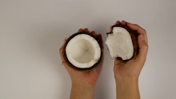Beautiful female hands holding vertically and open and close a broken coconut in studio lighting