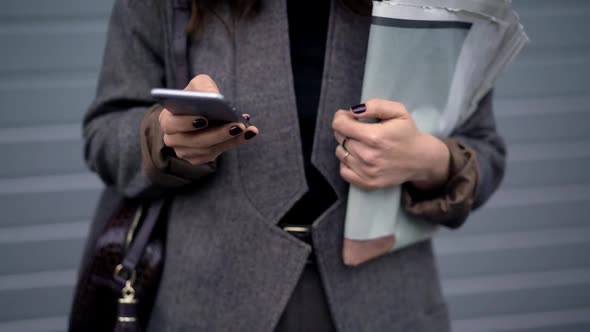 Pan Shot of Woman Holding Newspapers and Typing in the Phone alt