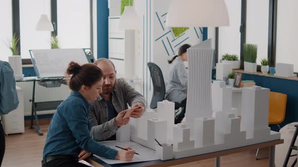 Colleagues Using Smartphone to Analyze Building Model and Blueprints Plan on Table alt