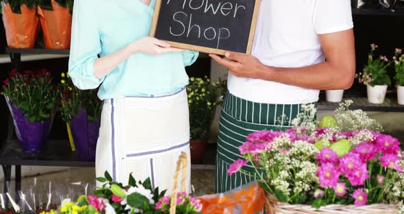 Smiling florists holding flower shop sign on slate in flower shop alt